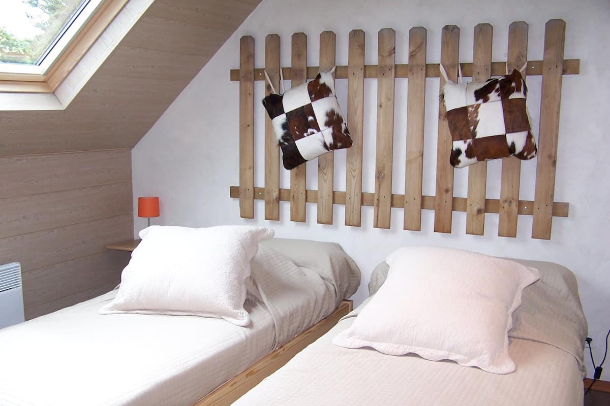Ein Schlafzimmer mit zwei Betten, einer Wanddekoration aus Holzleisten, einem kleinen Tisch und einem Fenster.