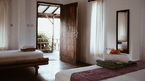 A room with two beds, a wooden door leading outside, and a large mirror on the wall. - El Jardin de Shambala (Gili Air)
