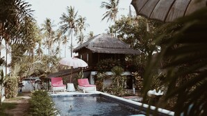 A pool area with lounge chairs and a thatched-roof structure. - El Jardin de Shambala (Gili Air)