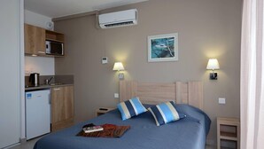 A hotel room with a bed, bedside lamps, a painting, a microwave, and a small kitchenette. - Relaxing Stay Near the Sea (Le Barcares)