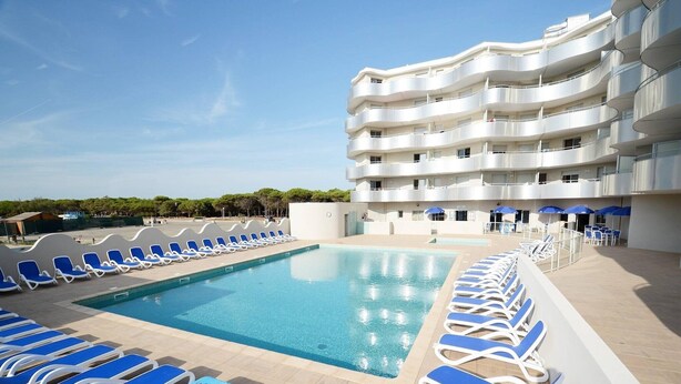 A swimming pool with sun loungers and a multi-story building with balconies. - Relaxing Stay Near the Sea (Le Barcares)