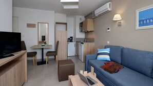 A modern living room with a flat-screen TV, a sofa, a coffee table, and a dining area with a table and chairs. - Relaxing Stay Near the Sea (Le Barcares)