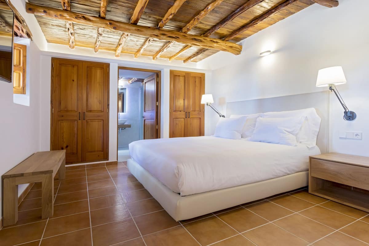 Ein Schlafzimmer mit Holzboden, einem Bett mit weißer Bettwäsche, zwei Nachttischlampen und einer Holzbank.