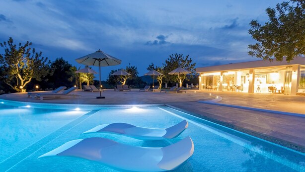 A swimming pool with lounge chairs and umbrellas, surrounded by trees and a building with outdoor seating. - Agroturismo Can Toni Xumeu - Only Adults (Santa Eulalia del Rio)