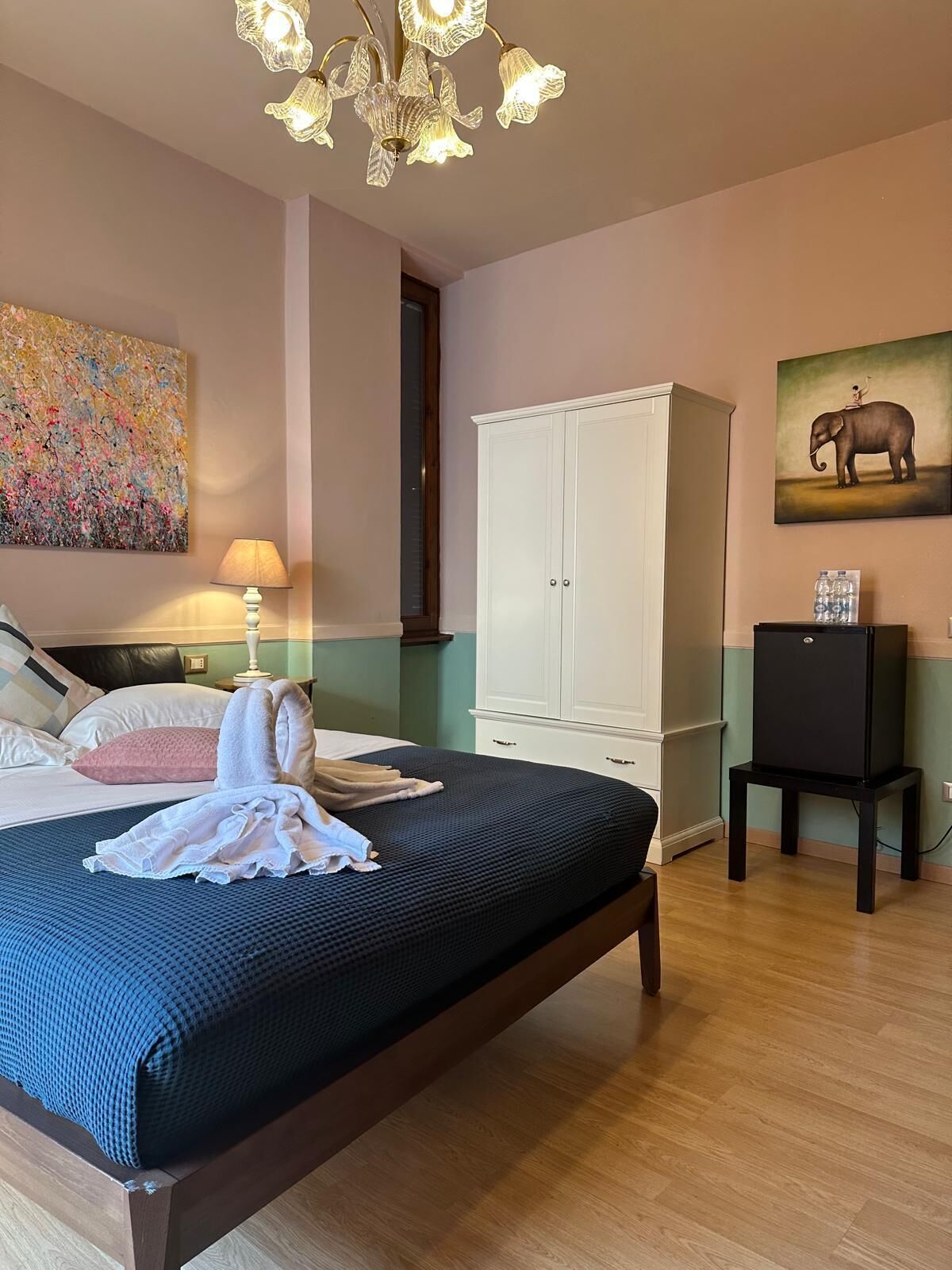 Ein Schlafzimmer mit einem Bett, einem weißen Kleiderschrank, einem Elefantenbild und einer Chandelieber.