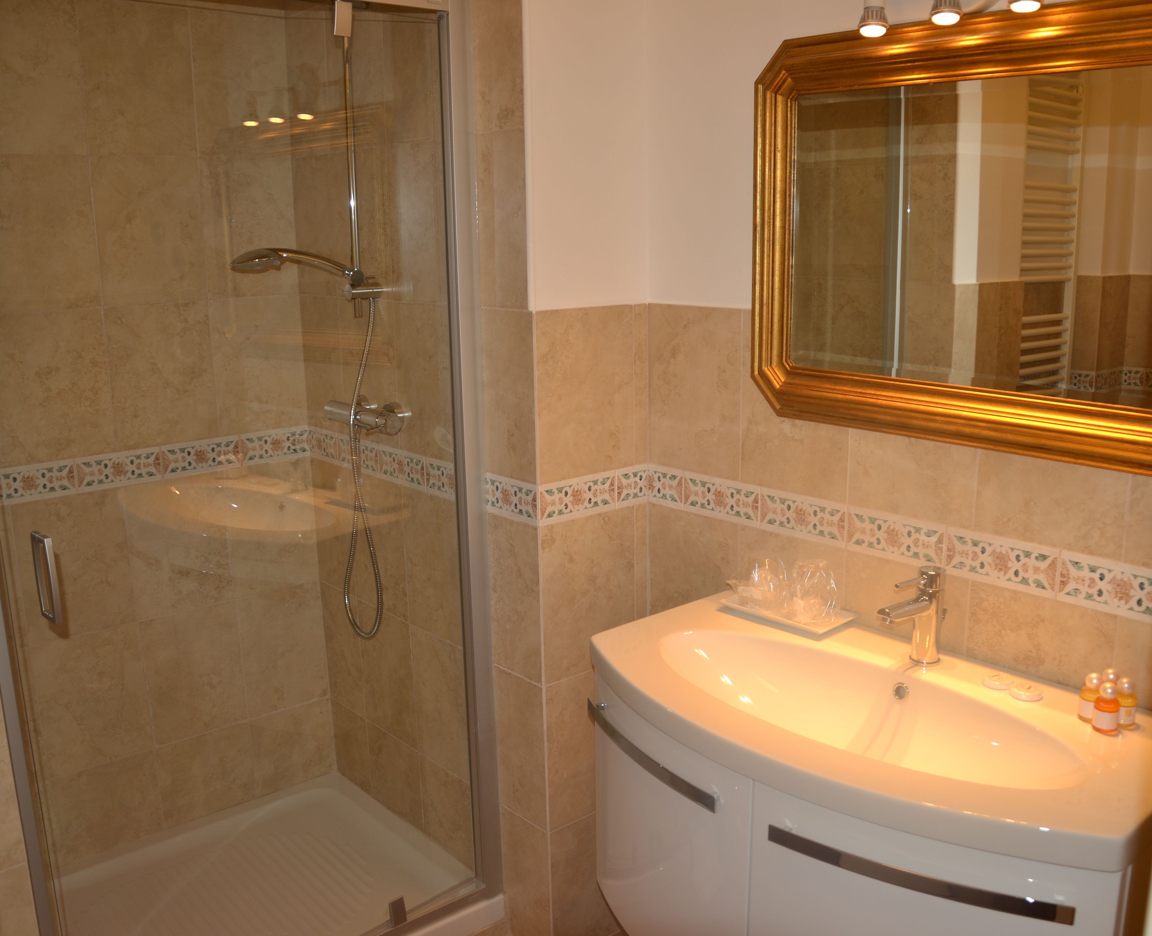 Ein Badezimmer mit einer Glaskabine zur Dusche, einem Waschbecken mit Spiegel darüber und dekorativen Fliesen entlang der Fußleisten.