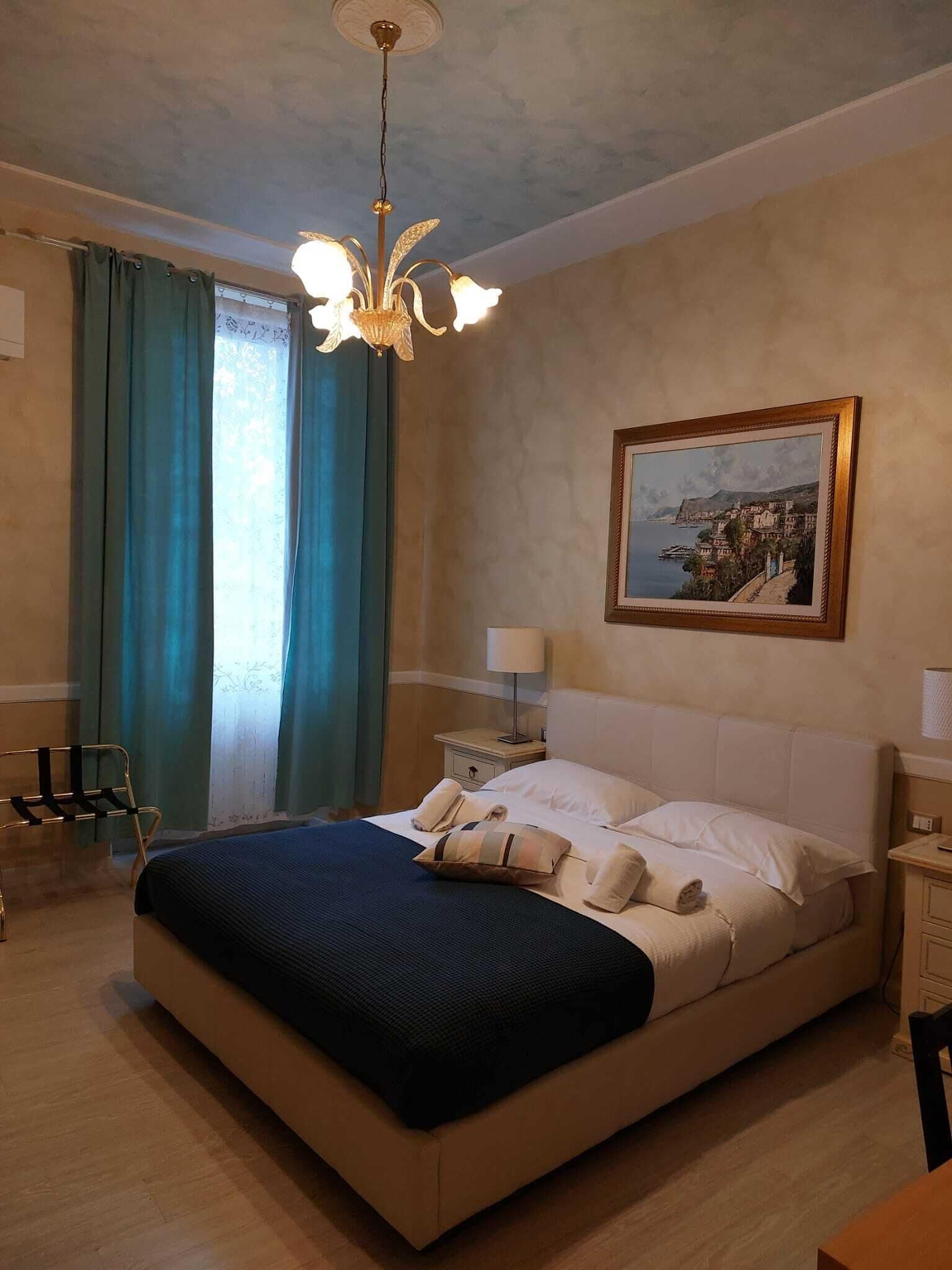 A bedroom with a large bed, a nightstand, a chair, a desk, and a painting on the wall.