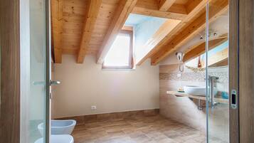 Un baño con tragaluz, vigas de techo de madera, un inodoro, un lavabo y una zona de ducha.