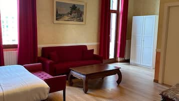 A hotel room with a bed, a red sofa, a wooden coffee table, and a chandelier.