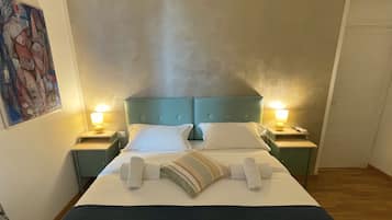 A neatly made bed with white linens and a striped pillow, two bedside lamps, and a painting on the wall.