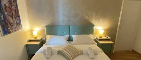 A neatly made bed with white linens and a striped pillow, two bedside lamps, and a painting on the wall.