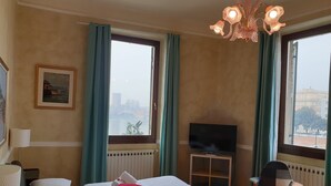 A hotel room with a bed, a television, a chair, and large windows with a view of a cityscape. - Lady Verona (Verona)