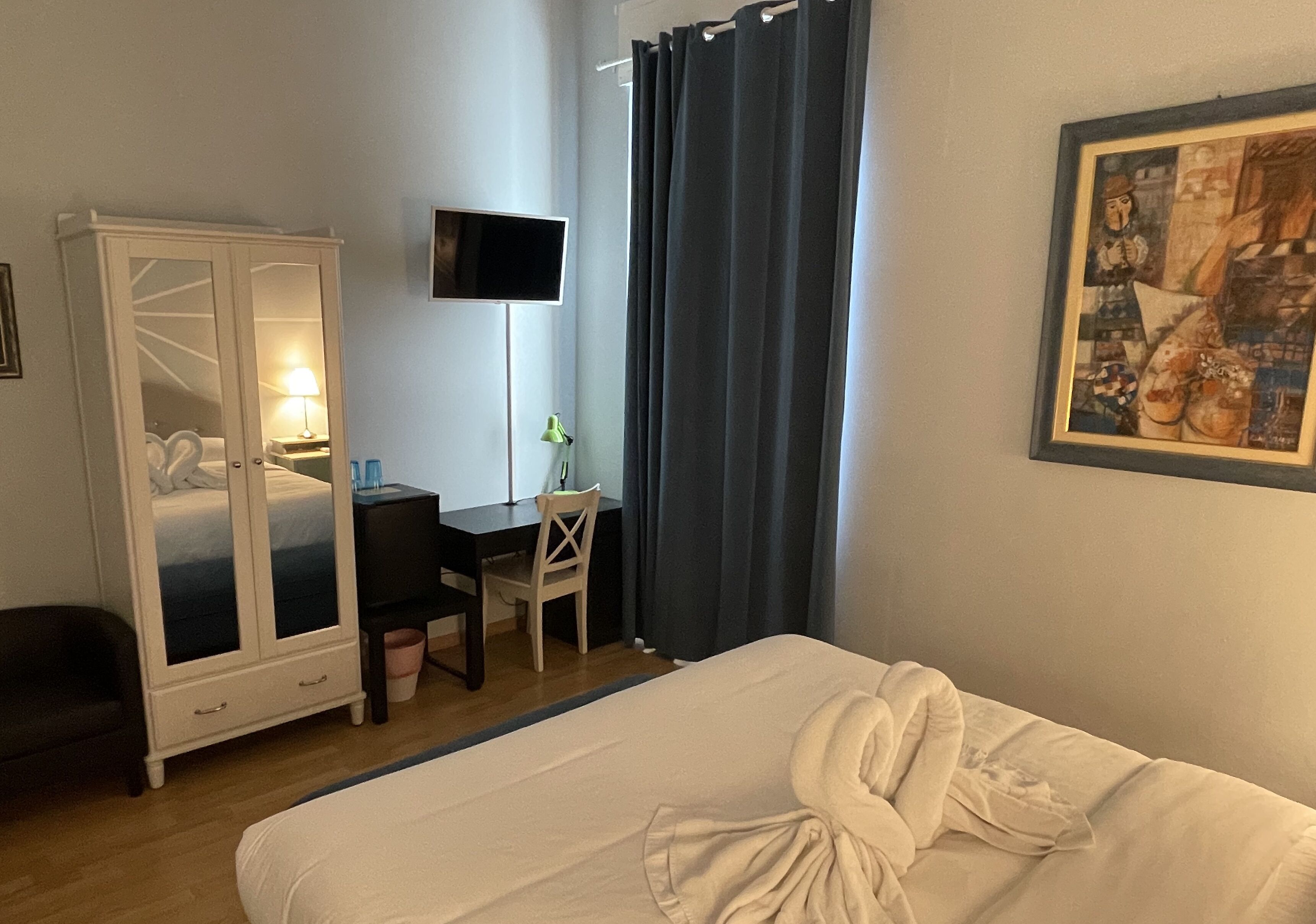 Een hotelkamer met een bed, een bureau, een stoel, een kledingkast, een televisie en een schilderij aan de muur.