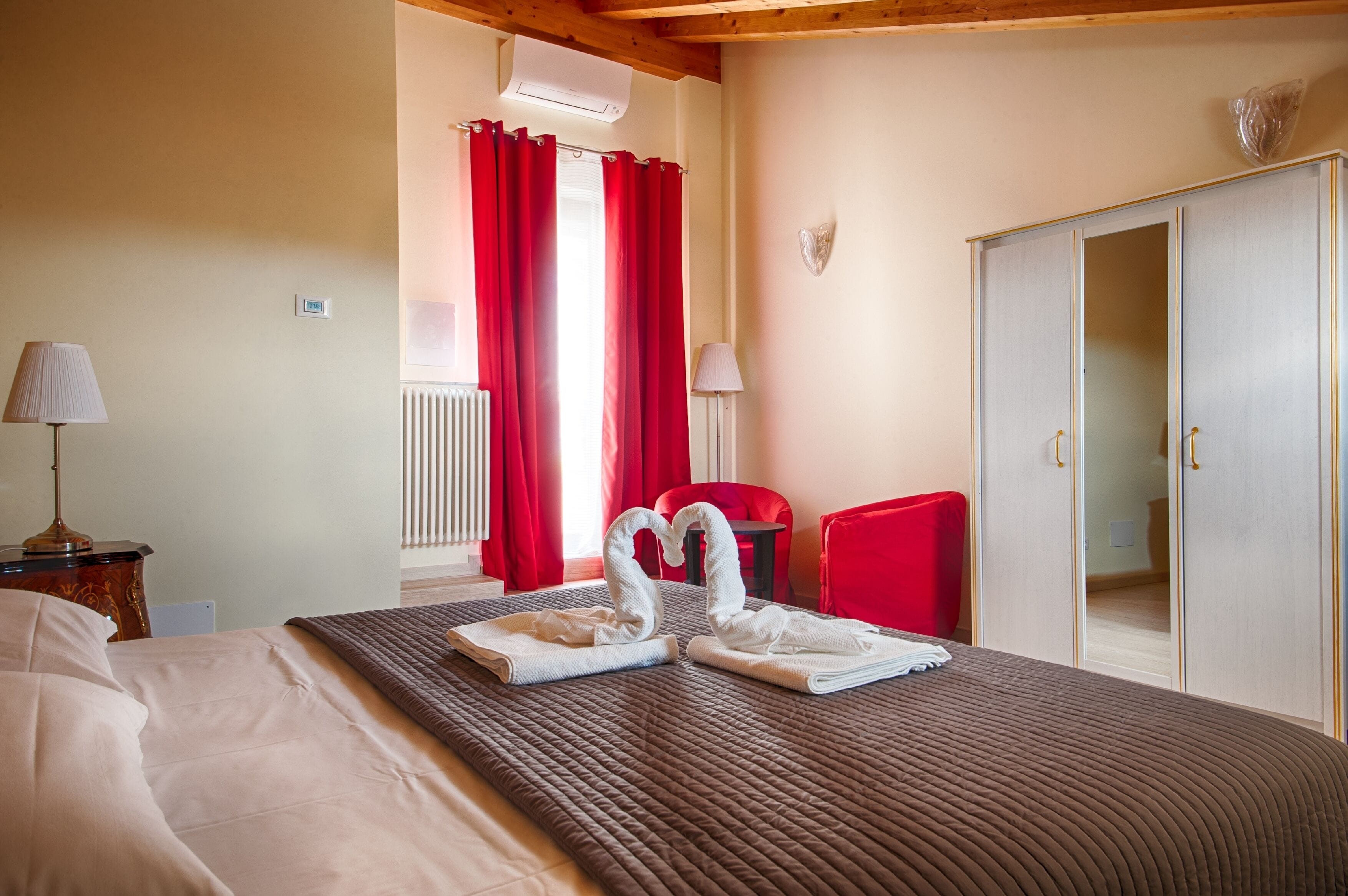 Una habitación de hotel con una cama, un armario, una silla roja y una mesa con una lámpara.