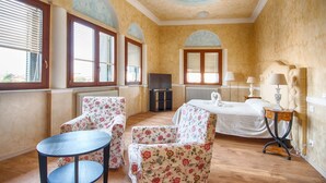 A hotel room with a bed, two floral armchairs, a small table, and a TV. - Lady Verona (Verona)
