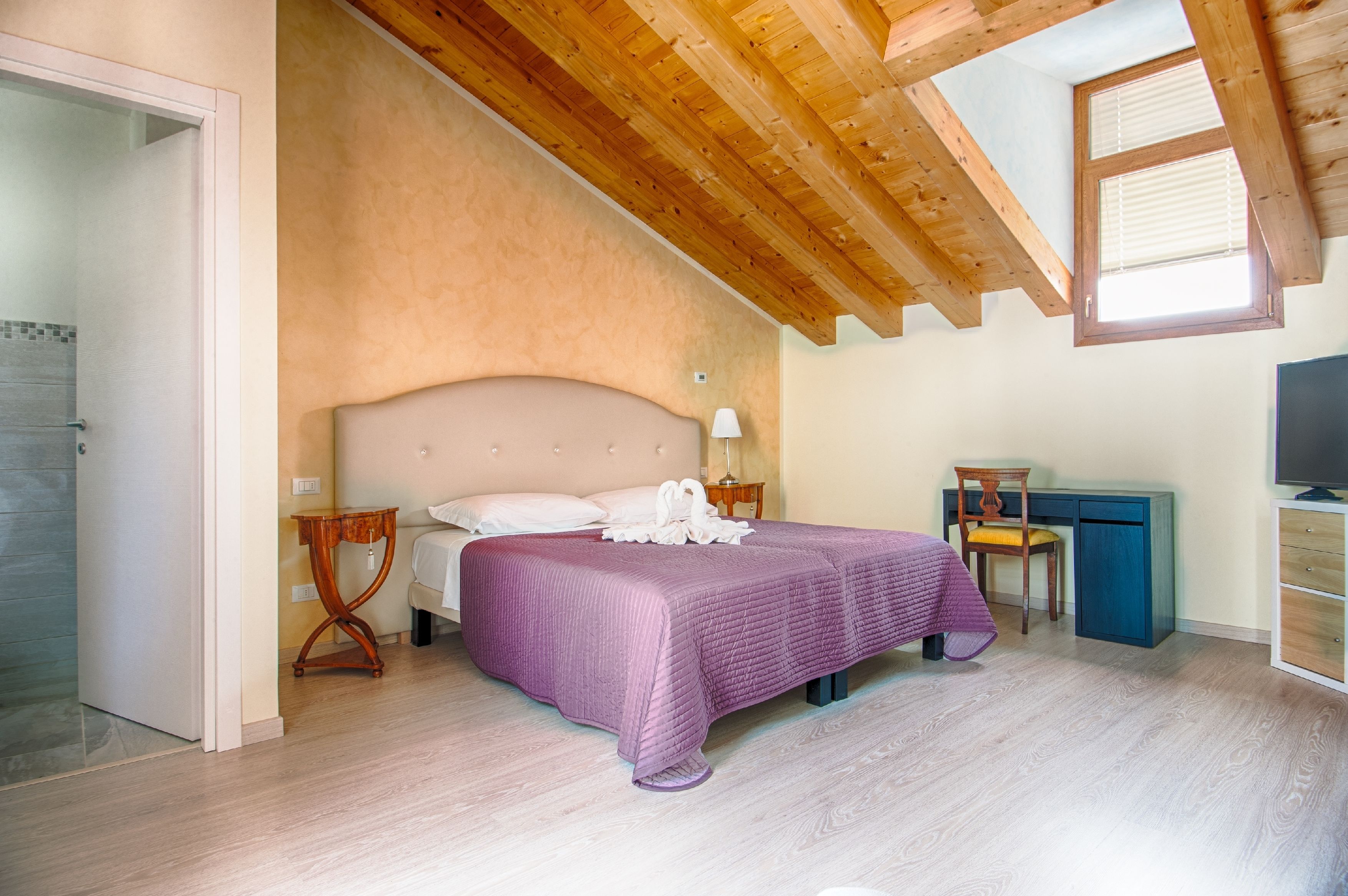 A bedroom with a bed, bedside table, lamp, desk, chair, and TV.