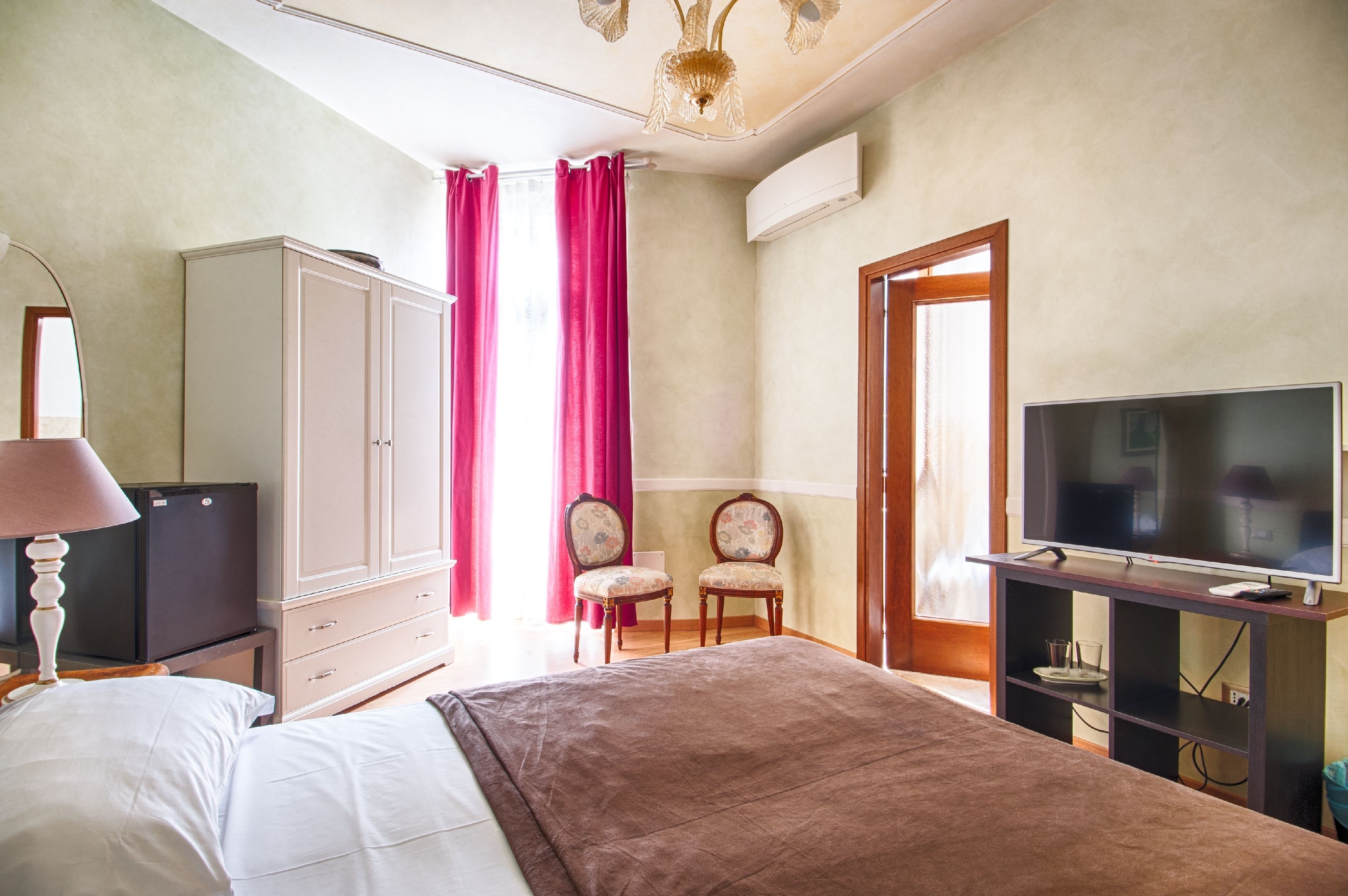 A bedroom with a bed, a television, a wardrobe, and two chairs.
