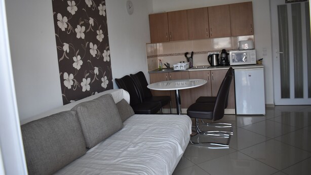 A compact living space with a sofa, a small dining table, and a kitchenette area. - Gréta Wellness Apartmanok -Köztársaság u (Siófok)