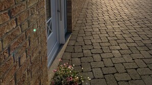 Un bâtiment en briques avec une porte et un chemin pavé menant à un champ d’herbe.
