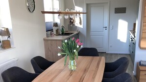 Un coin repas avec une table en bois et six chaises sombres, un vase avec des fleurs, et une cuisine en arrière-plan.