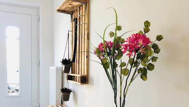 Un couloir avec un banc en bois, une table ronde ornée d’un vase de fleurs et un miroir fixé au mur.