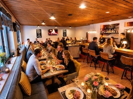 Restaurante com teto de madeira, mesas com velas e um espaço de bar.