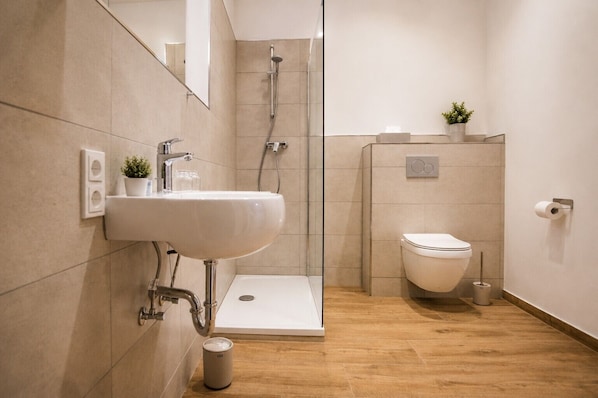 A modern bathroom with a sink, toilet, shower, and a small potted plant. - Hotel Wiesengrund (Dinklage)