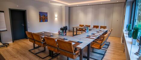 A modern conference room with a long table, wooden chairs, and a whiteboard.