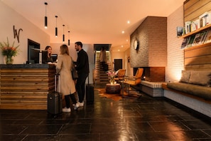 Un vestíbulo de hotel con mostrador de recepción, chimenea, zona de estar y una escalera.