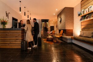 Um lobby de hotel com balcão de recepção, lareira, área de estar e escadaria.