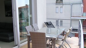 A balcony with a glass table and wicker chairs, a sliding glass door, and a view of a building. - Gréta Wellness Apartmanok - Szt László u (Siófok)