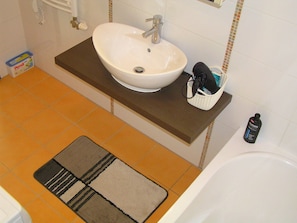 A bathroom with a white sink, a small basket, and a bottle of shampoo on a counter. - Gréta Wellness Apartmanok - Szt László u (Siófok)