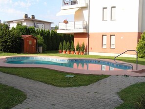 A swimming pool with a metal ladder, surrounded by a paved walkway and grass. - Gréta Wellness Apartmanok - Szt László u (Siófok)