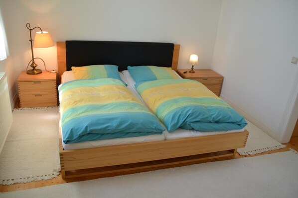 A double bed with a wooden frame and a black headboard, flanked by two bedside tables with lamps.