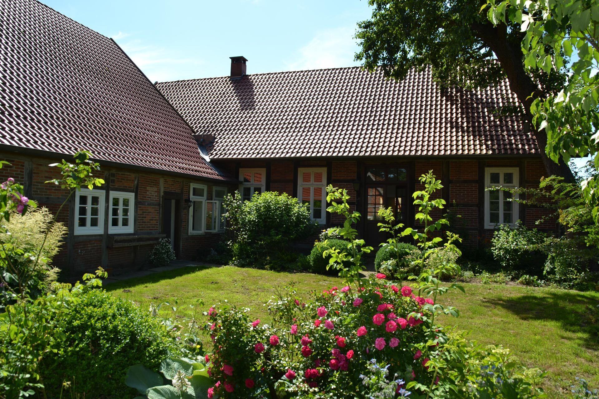 Une maison traditionnelle en briques, avec un toit en tuiles et un jardin bien entretenu, agrémenté de plantes à fleurs.