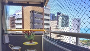 Un balcón con una maceta, dos taburetes y vistas de edificios circundantes.
