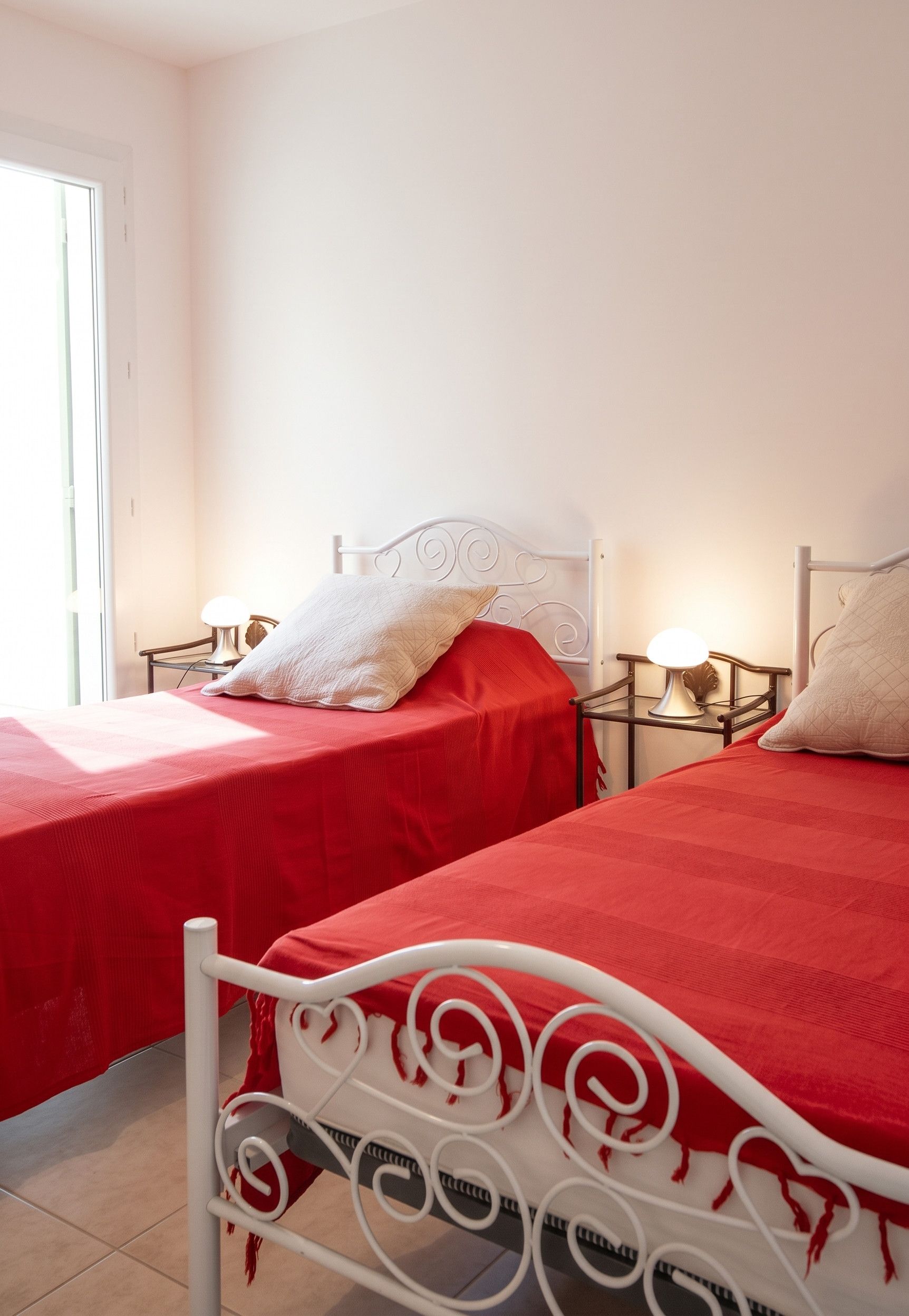Een slaapkamer met twee bedden, elk met een rode sprei en witte kussens, en een wit metalen hoofdbord.