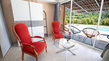 Una habitación con dos sillones tapizados en rojo, una mesa de vidrio y vistas a una piscina y vegetación al exterior.