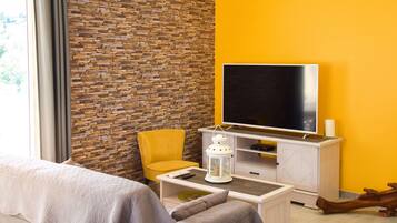Een moderne kamer met een bakstenen muur, een geel accentkleur, een flatscreen televisie, een gele fauteuil, een witte salontafel en een bed met een witte dekbedovertrek.