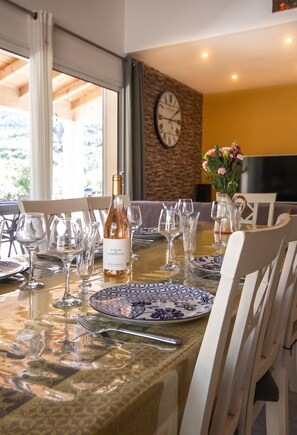 A dining table set with wine glasses, plates, and cutlery, a bottle of wine, and a clock on the wall. - Homerez - House, La Roche-sur-le-Buis. (La Roche-sur-le-Buis)