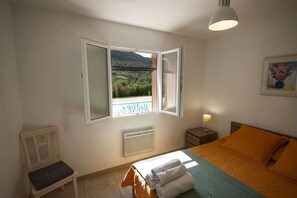 Ein Schlafzimmer mit Bett, Fenster, Sessel, Nachttisch und einem Gemälde.