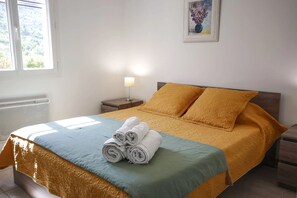 Una cama bien hecha con toallas enrolladas, una lámpara de noche y un cuadro en la pared.