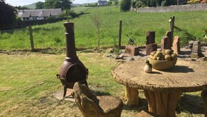 A rustic outdoor setting with a wood-burning stove, a round wooden table, and a bowl of potatoes. - Vollie House (Thornhill)