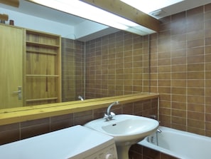 Un baño con tocador de madera, lavamanos, espejo y bañera.
