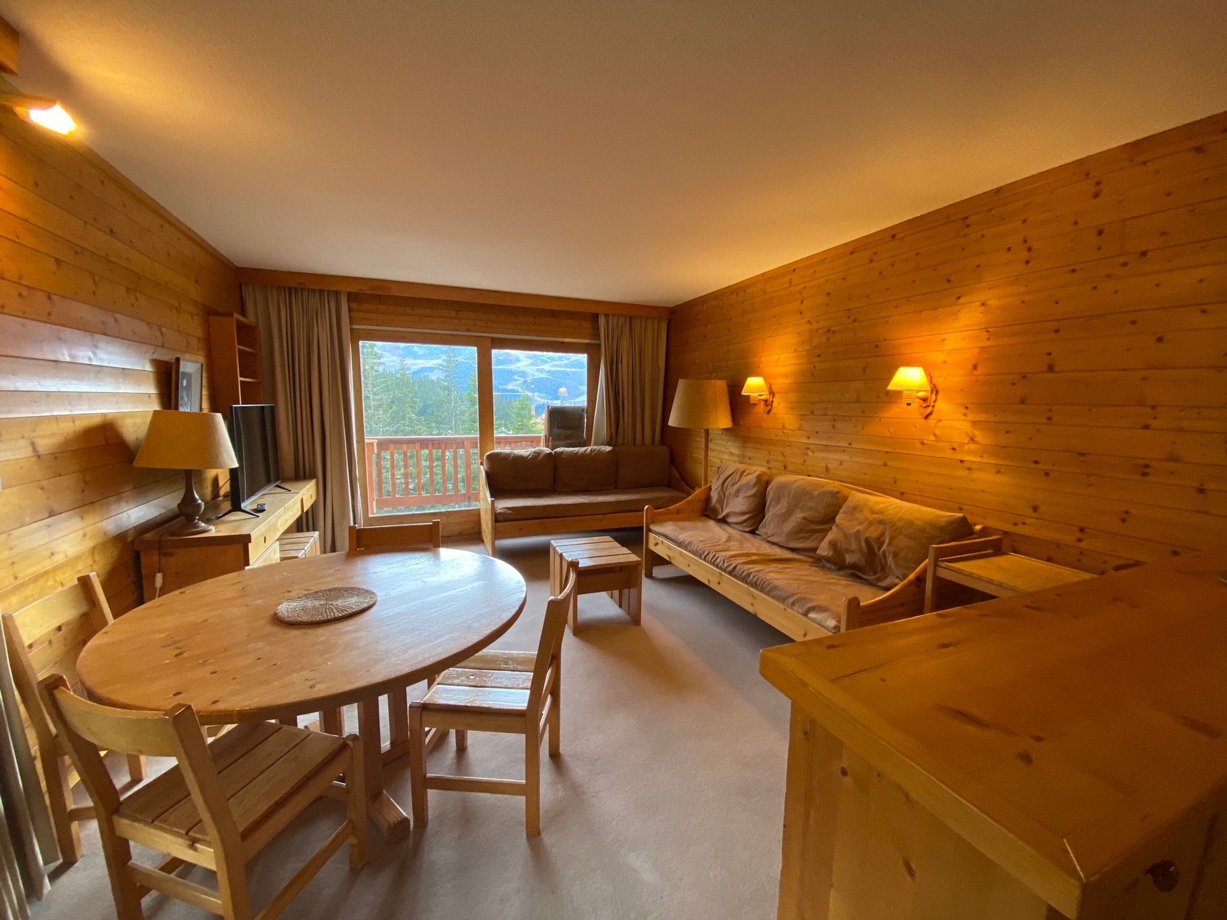 Un intérieur en bois avec une table de salle à manger ronde, deux canapés et un téléviseur.