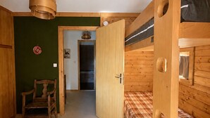 Ein Zimmer mit einem Etagenbett, einem Holzhocker, einer Tür zu einem anderen Raum und einer Pendelleuchte.