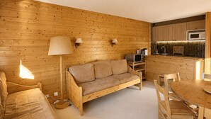 Ein gemütliches Zimmer mit Holzboden, einer Couch, einem Tisch mit Stühlen, einer Lampe und einer Küchenzeile mit Schränken und einer Mikrowelle.