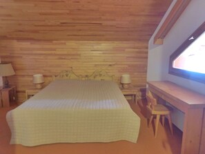 A bedroom with a wooden headboard, a bed with a quilt, two bedside lamps, a desk with a chair, and a window with a view. - Sunny 2/3 room apartment for 6 people in Méribel Altiport (Méribel)