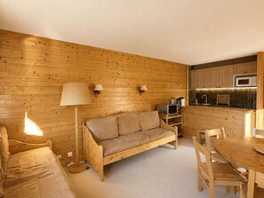 Una habitación acogedora con suelo de madera, un sofá, una mesa con sillas, una lámpara y una kitchenette con armarios y un microondas.