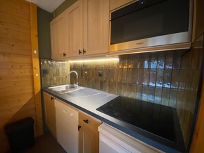 Cozinha moderna com armários de madeira, pia de aço inoxidável e micro-ondas embutido.